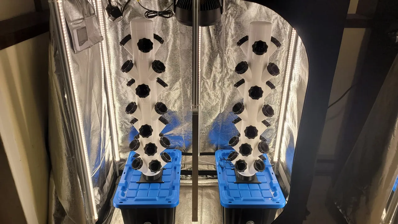 Two white 3D-printed hydroponic towers studded with black grow pods, lit by LED bars in grow tents