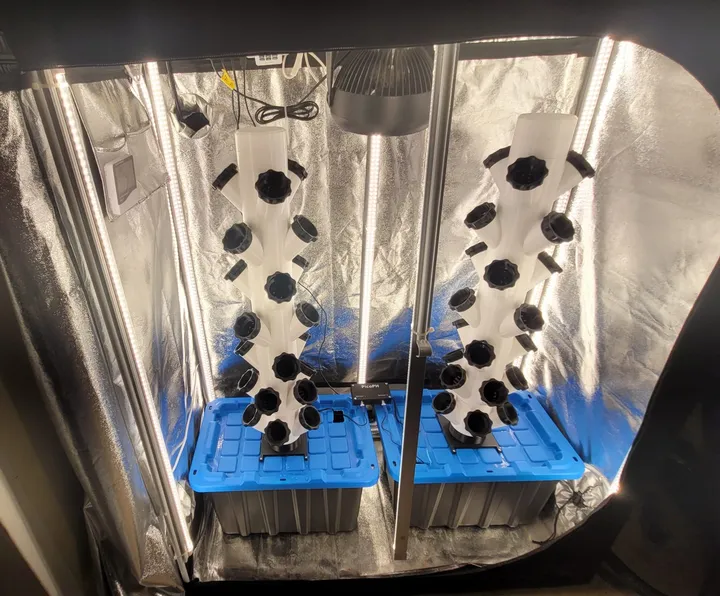 Two vertical tower gardens growing greens inside a reflective grow tent