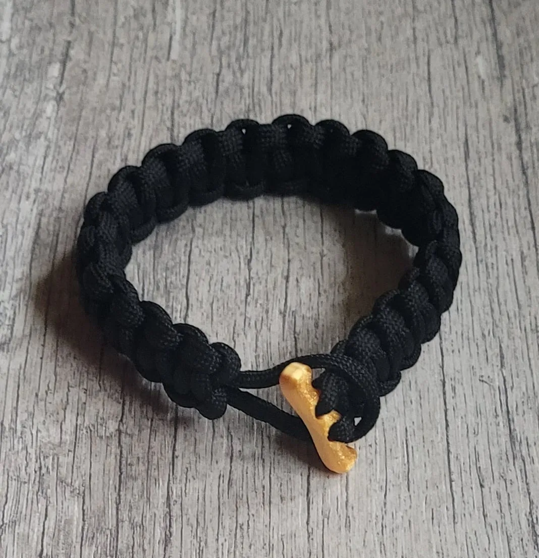 A black paracord bracelet fastened with a printed gold buckle