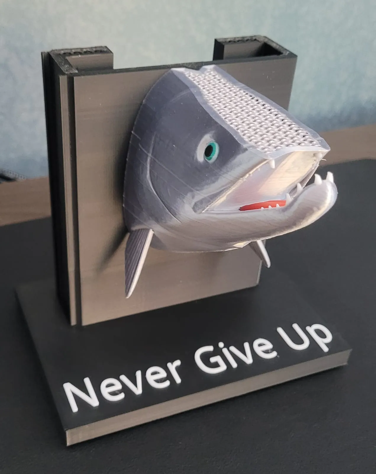 A 3D-printed salmon head wall-mount on a "Never Give Up" base