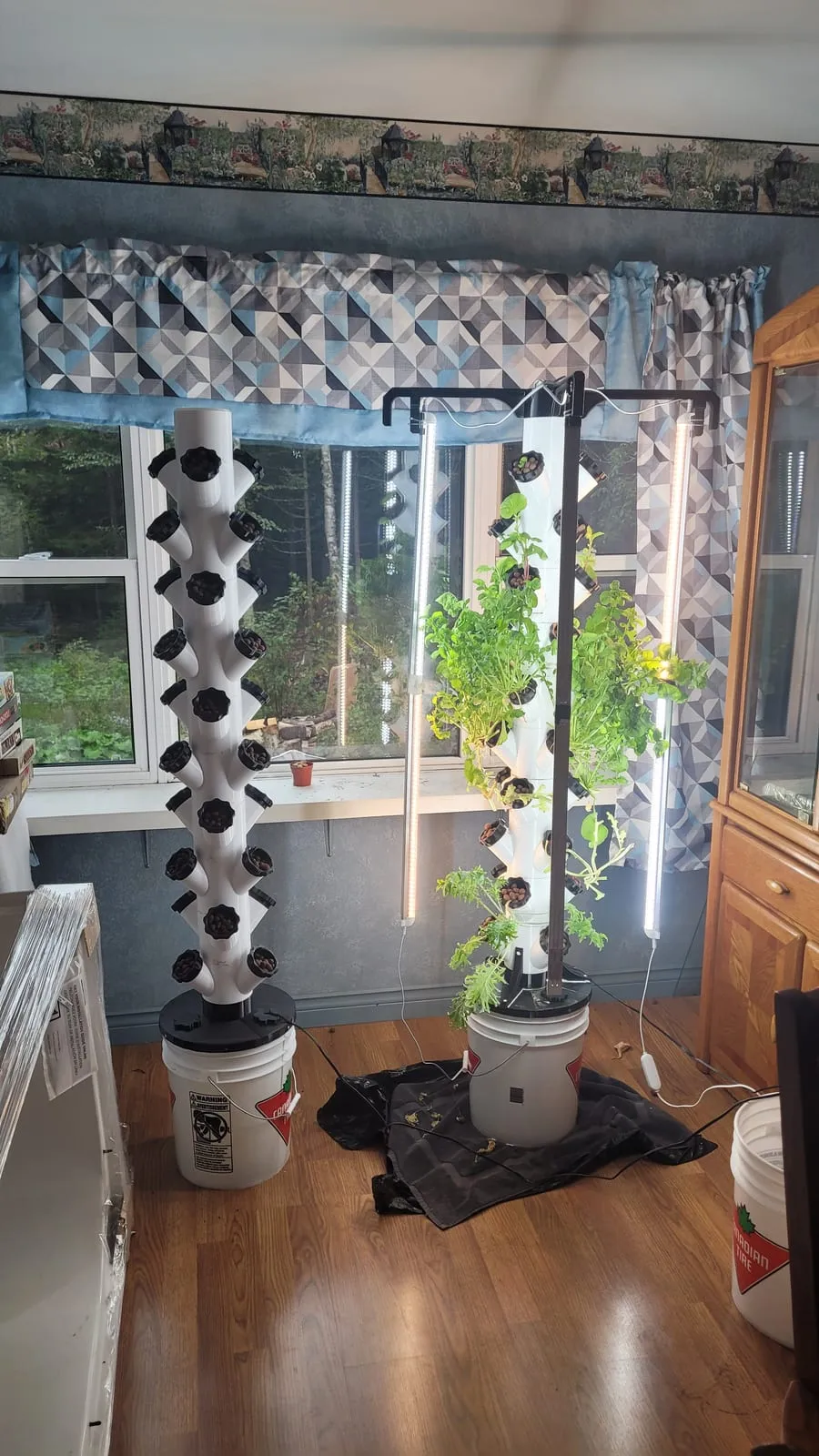 A vertical hydroponic tower garden under grow lights in the room